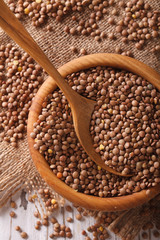 Raw brown lentils in a wooden bowl close-up. Vertical top view
