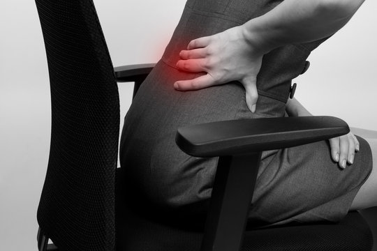 Young businesswoman having back pain while sitting at office des