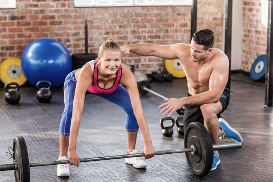 Woman lifting barbell with her trainer