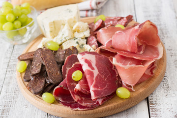 Antipasto catering platter with bacon, jerky, sausage, blue cheese and grapes on a wooden background
