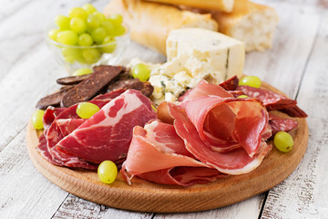 Antipasto catering platter with bacon, jerky, sausage, blue cheese and grapes on a wooden background