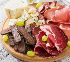 Antipasto catering platter with bacon, jerky, sausage, blue cheese and grapes on a wooden background