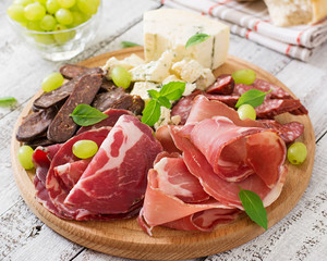 Antipasto catering platter with bacon, jerky, sausage, blue cheese and grapes on a wooden background