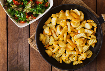 Frying pan with a fried potato in a rural way on a wooden background