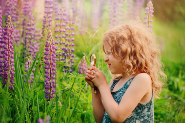 cute child girl exploring nature with loupe on summer flower field