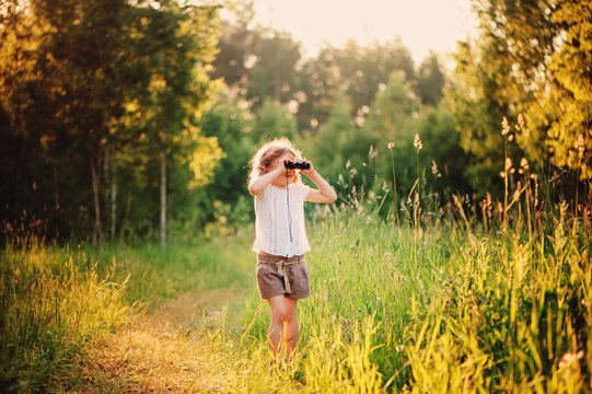 child girl watching birds with binocular on the walk in summer sunny forest