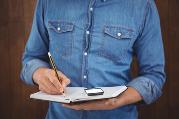 Mid section of hipster with mobile phone writing on book