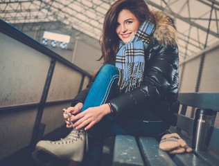 Cheerful girl putting on skates  on ice skating rink