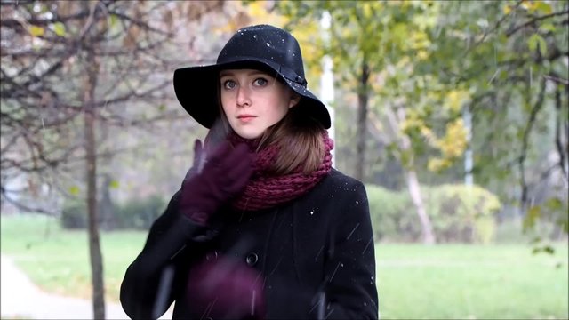 Осень. Первый снег. Портрет девушки. Девушка красивая, в шляпе и пальто. Девушка сильно замерзла, ей холодно. Девушка ждет. Ожидание. Парк осенний, идет снег 