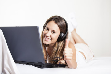 Girl with headphones listening to the music in a laptop on the bed at home