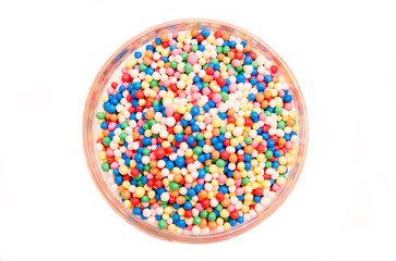 Balls of colored sugar on bowl on a white background seen from above