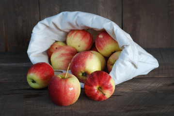Red apples in a cloth bag on a wooden background.