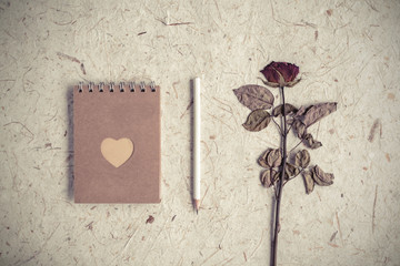 Single dried rose flower with notebook on mulberry paper