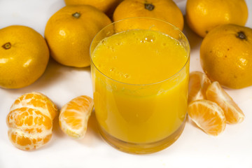 Glass of orange juice beside tangerines and peeled mandarin segments