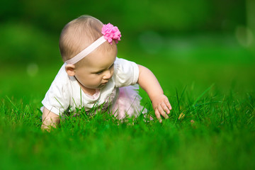 A little baby in the pink dress crawls on a grass