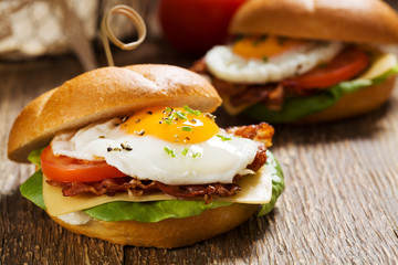 Sandwich with a fried egg, bacon, cheese and vegetables.
