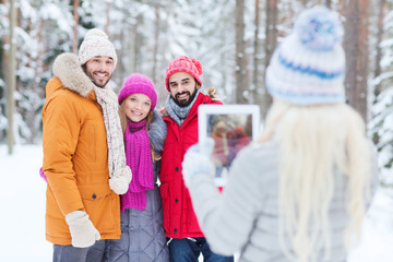 smiling friends with tablet pc in winter forest