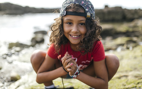 Spain, Gijon, portrait of smiling little girl crouching at rocky coast
