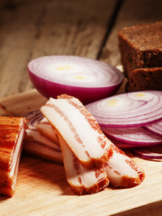 Smoked bacon with red onion and rye bread on a cutting board, se