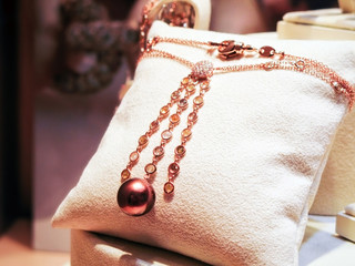 Necklace made of pink gold with diamonds and gems on a stand.