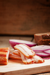 Smoked bacon with red onion and rye bread on a cutting board, se