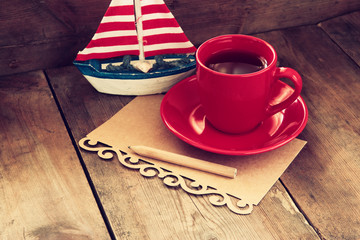 red cup of tea and letter paper next to vintage decorative boat on wooden old table. retro filtered...