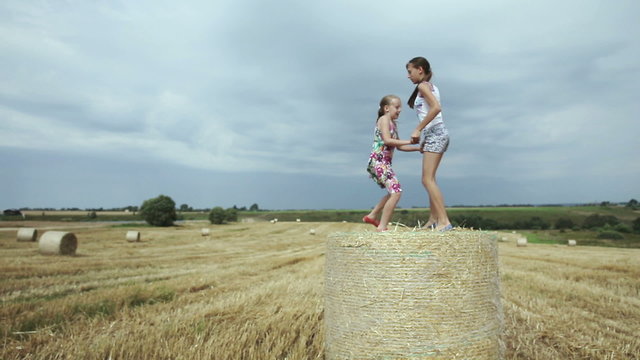 Two girls jump on haystack.