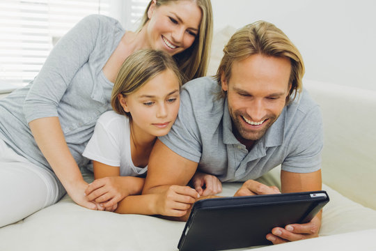 Happy father, mother and daughter lying on couch sharing digital tablet