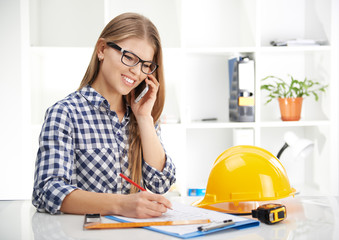 Young female architect consultant talking on phone in the office. Woman designer working on...