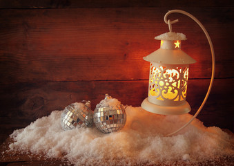 christmas background with white lantern, bauble and snow over wooden background
