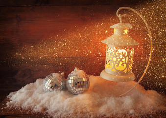 christmas background with white lantern, bauble and snow over wooden background
