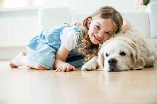 Little girl cuddling with her dog, lying on floor