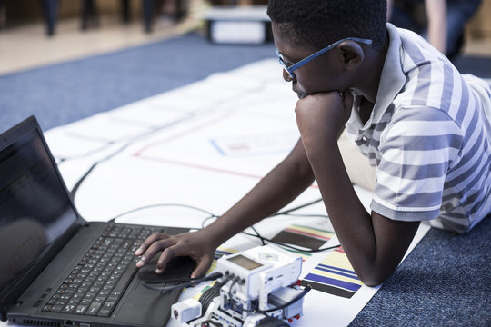 Schoolboy with laptop in robotics class testing vehicle on test track