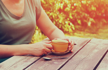 close up image of woman drinking coffee outdoors, next to wooden table at afternoon. filtered image. selective focus
