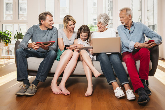 Group picture of three generations family with different digital devices sitting on one couch
