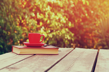 Naklejka na ściany i meble coffee cup mug and book over wooden table outdoors, at afternoon time. selective focus 