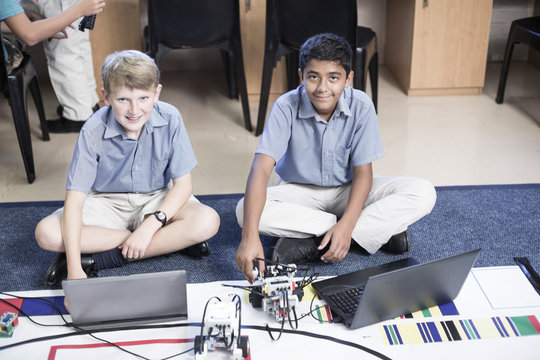 Two smiling schoolboys with laptops in robotics class