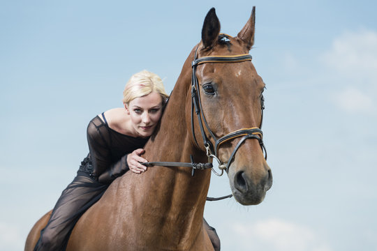 Portrait of young woman wearing black clothes sitting on horse