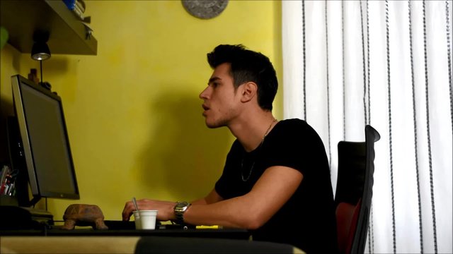 Young man sitting at desk at home using a computer, smoking cigarette then relaxing while working