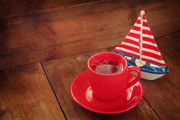 red cup of tear next to vintage decorative boat on wooden old table. retro filtered image
