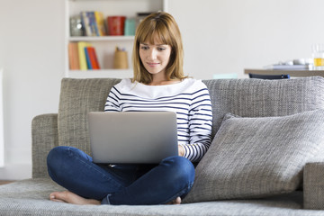Mid adult woman on her sofa using laptop at home.