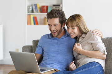 Happy successful young couple with laptop on sofa in modern apartment