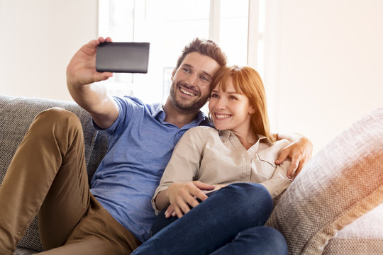 Lover couple taking a selfie with mobile phone at home on sofa