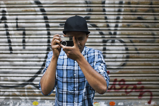 Young man with baseball cap taking photos in front of roller shutter
