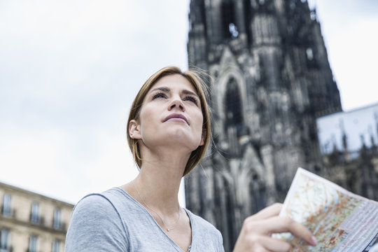 Germany, Cologne, portrait of young woman with city map in front of Cologne Cathedral