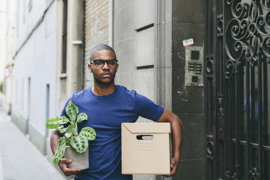 Spain, Barcelona, portrait of young man with cardboard box and foliage plant in front of a house