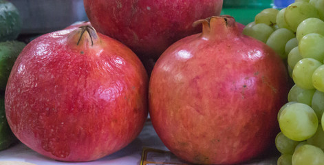 fresh red Pomegranates stacked with grapes in store for purchase
