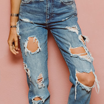 lady in fashionable ripped jeans stands in pink wall