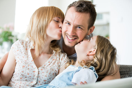 Happy family sitting on couch, mother and daughter kissing father