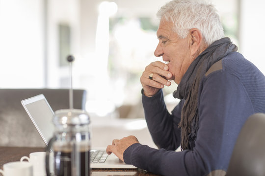 Senior man with laptop and coffee pot at home